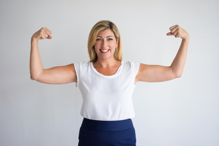 Happy Mature Caucasian Woman Flexing Biceps, wondering about menopause.