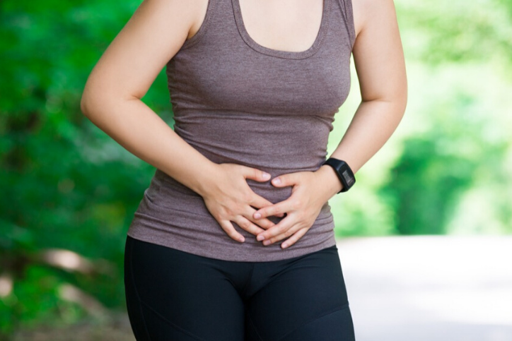 Woman with Endometriosis pain holding her stomach in a park.