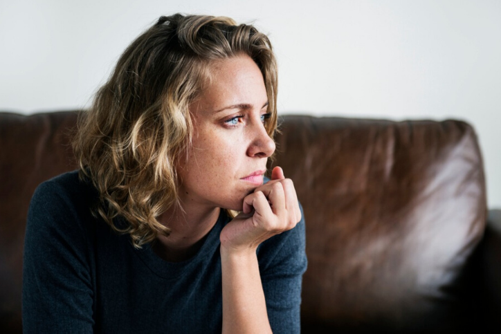 young Caucasian woman sitting on leather sofa worried about irregular menstrual bleeding.