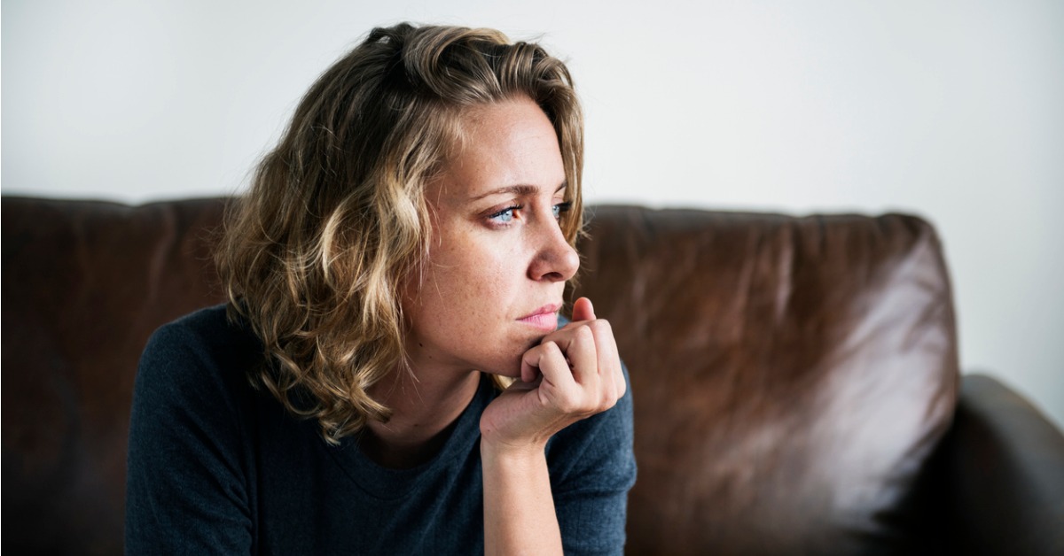 young Caucasian woman sitting on leather sofa worried about irregular menstrual bleeding