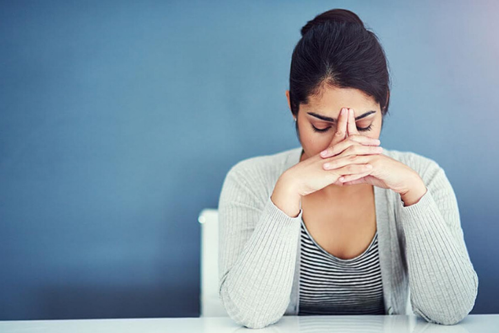 Woman leaning into her hands, looking stressed out, wondering about how stress impacts your period.