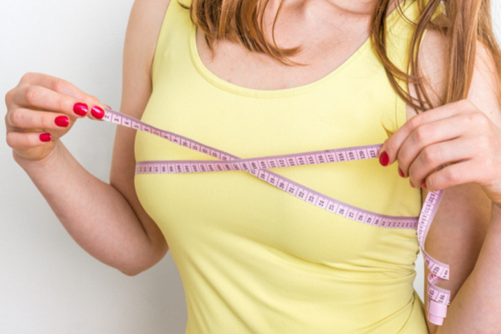 A woman wearing a yellow tank top with tap measure around her breasts, trying to figure out the right bra size for you.