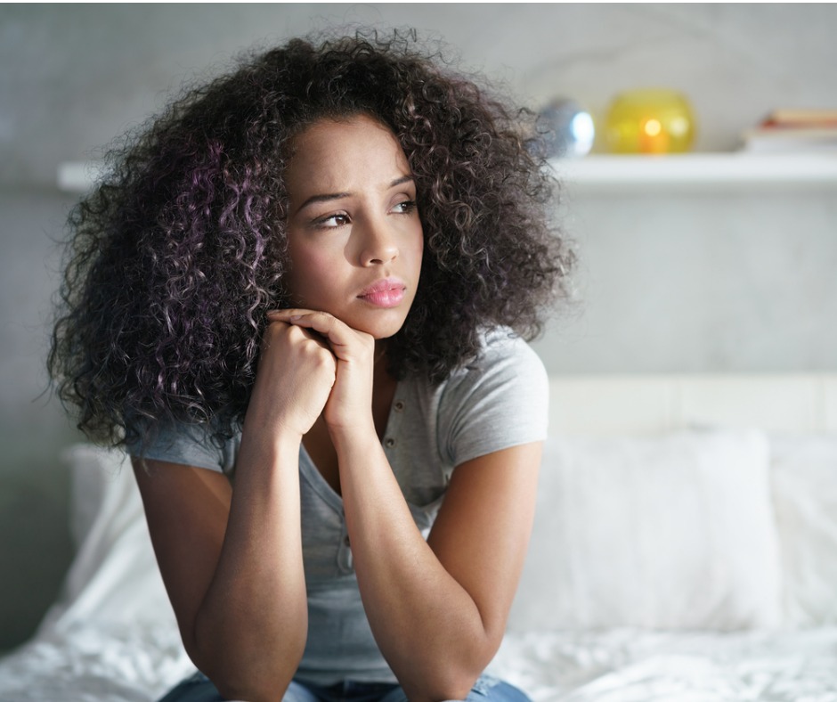 Young latina woman with Polycystic Ovary Syndrome sitting on bed.