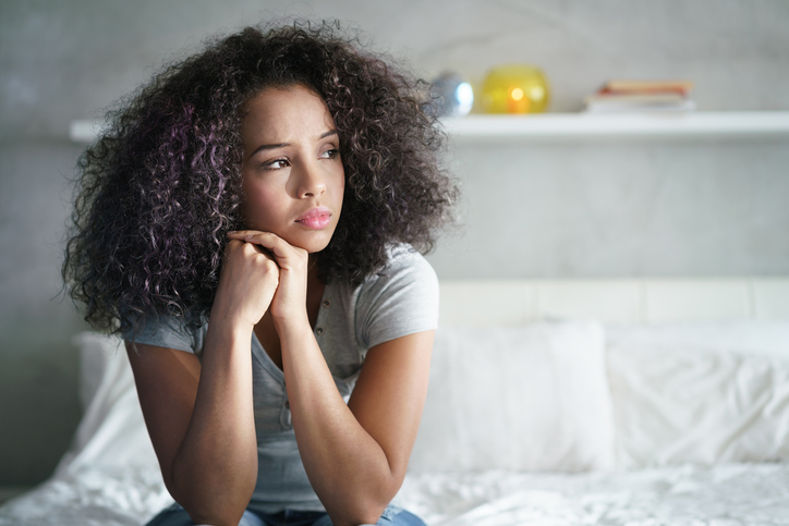 Young latina woman with Polycystic Ovary Syndrome sitting on bed., wondering about the mental issues women face.
