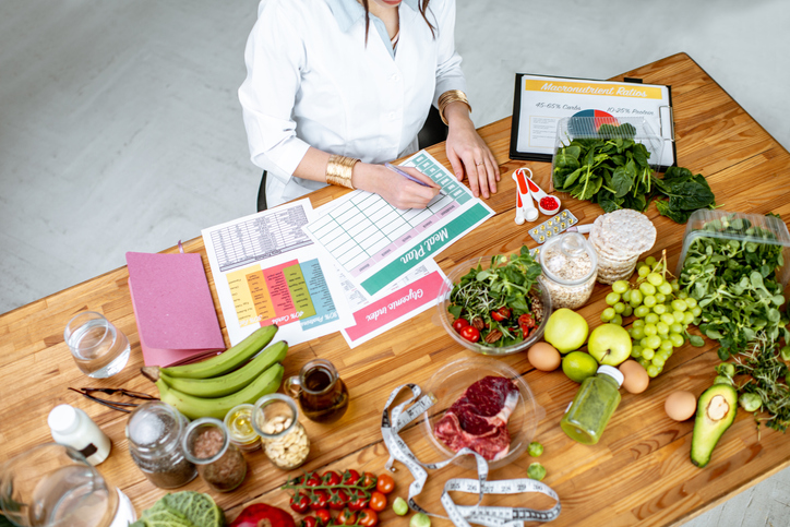 Dietitian writing a diet plan, view from above on the table with different healthy products and drawings on the topic of healthy eating