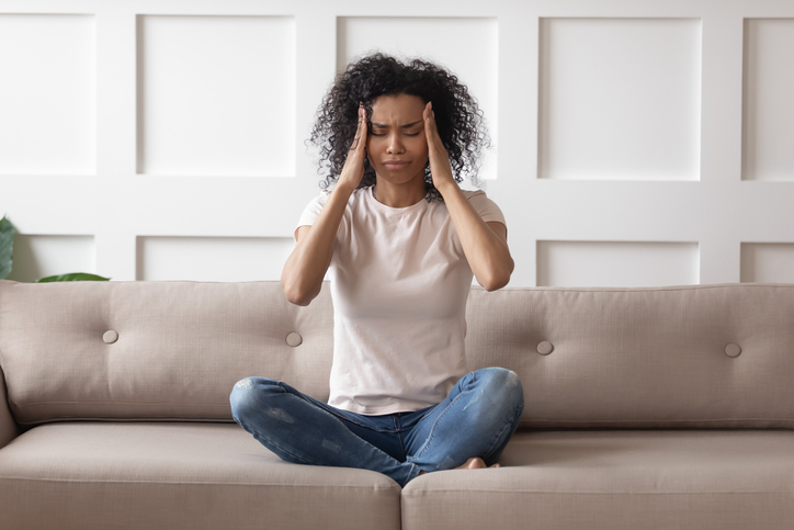 Upset stressed young african woman massage temples from women's hormones feel strong headache concept, frustrated tired black girl touching aching head suffer from migraine high blood pressure sitting on sofa at home