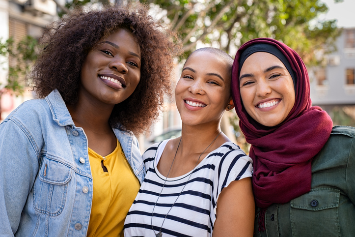 Group of three happy multiethnic friends looking at camera. Portrait of young women of different cultures enjoying vacation together. Smiling islamic girl with two african american friends outdoor., wondering about common Health Issues Women Face in their 20s