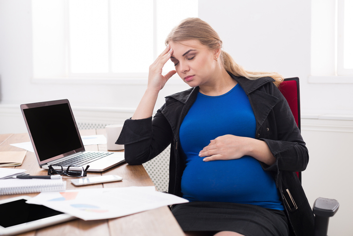 Tired pregnant businesswoman at office copy space. Expectant business lady feeling sick at work, wondering how stressful times can impact your pregnancy.