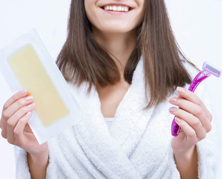 Portrait of young woman is choosing unwanted hair removal tool. Girl is holding disposable razor and wax stripe, wondering The Benefits of Keeping Your Pubic Hair.