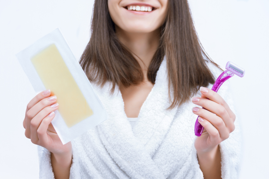 Portrait of young woman is choosing unwanted hair removal tool. Girl is holding disposable razor and wax stripe, wondering The Benefits of Keeping Your Pubic Hair.
