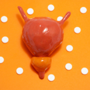 Model or figure of urinary bladder and prostate, which corresponds to anatomical original is located in orange background surrounded by white pills ornamented in polka dots, highlighting Overactive Bladder.