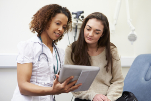 Nurse Showing Patient Test Results On Digital Tablet In Clinic Sitting Down, discussing with a young patient how to prepare for your first OBGYN visit.