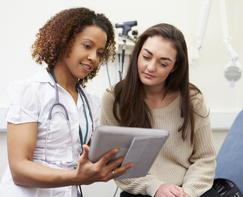 Nurse Showing Patient Test Results On Digital Tablet In Clinic Sitting Down, discussing with a young patient how to prepare for your first OBGYN visit.