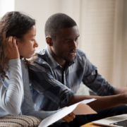 African Millennial stressed married couple sitting on sofa at home checking unpaid bills, taxes, due debt, bank account balance. Bankruptcy, debt and lack of money financial problems in family concept, wondering how stress impacts your sex life.