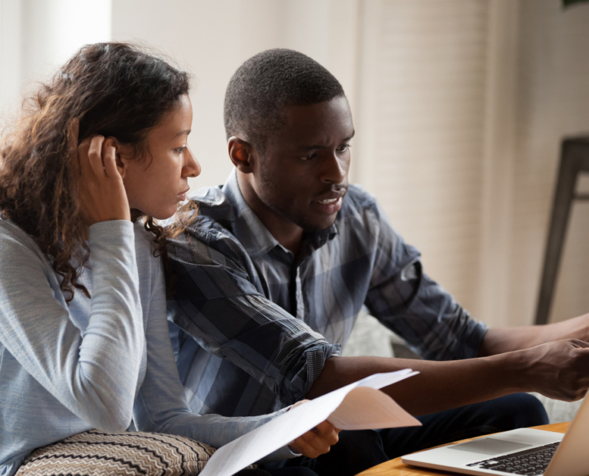 African Millennial stressed married couple sitting on sofa at home checking unpaid bills, taxes, due debt, bank account balance. Bankruptcy, debt and lack of money financial problems in family concept, wondering how stress impacts your sex life.