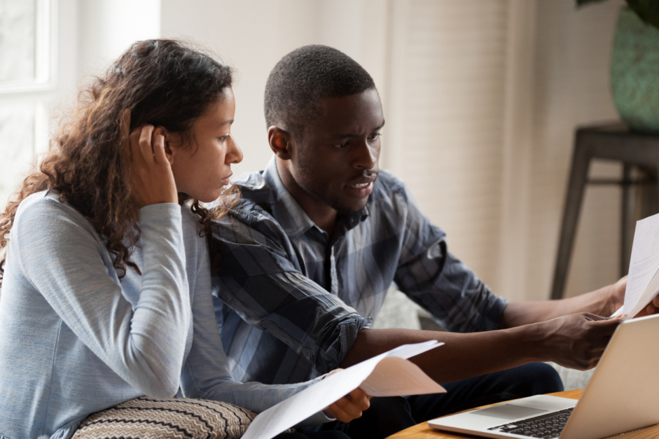 African Millennial stressed married couple sitting on sofa at home checking unpaid bills, taxes, due debt, bank account balance. Bankruptcy, debt and lack of money financial problems in family concept, wondering how stress impacts your sex life.