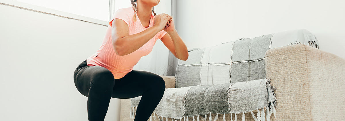 Young woman doing squats in living room