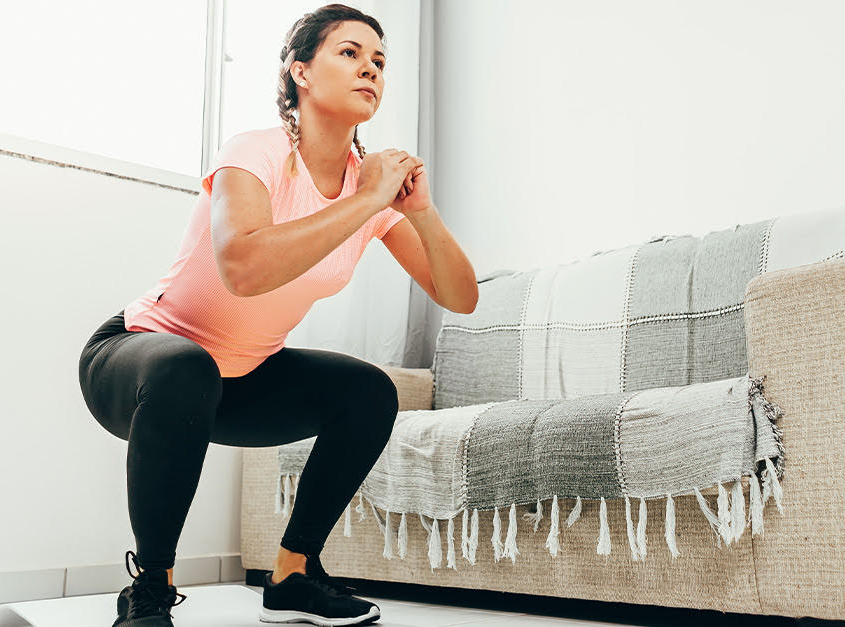 Young woman doing squats in living room