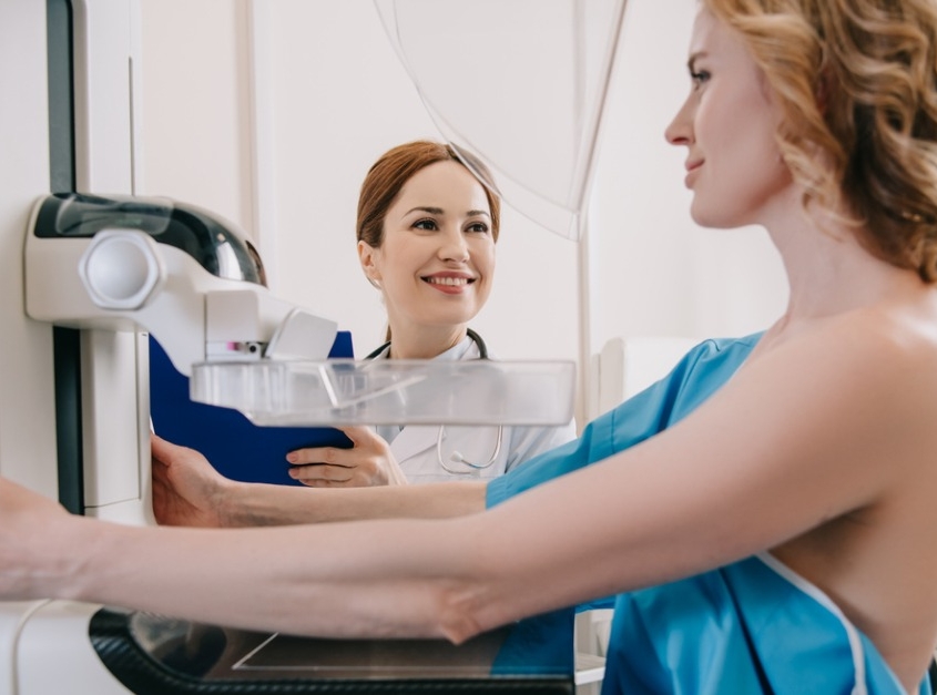 Smiling radiologist standing near patient while making mammography