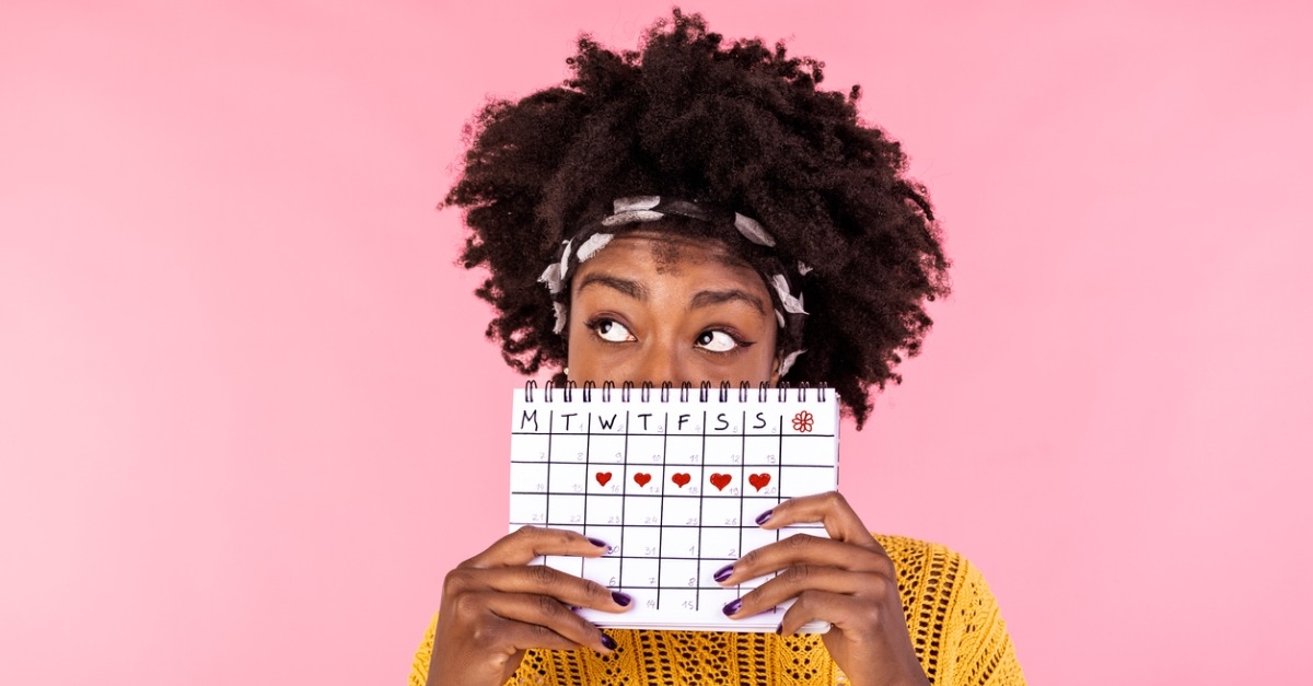portrait of a young african american girl hiding part of her face behind a calendar