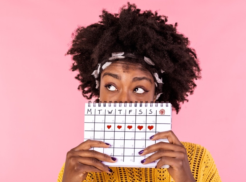 portrait of a young african american girl hiding part of her face behind a calendar