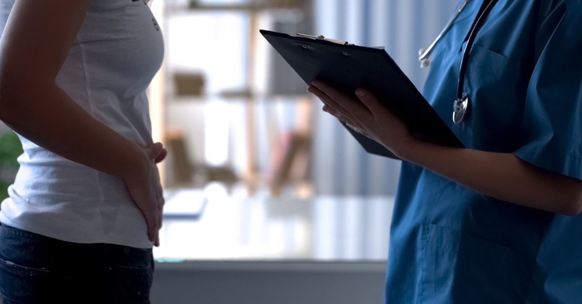 Young lady speaking to doctor while holding lower abdomen in pain