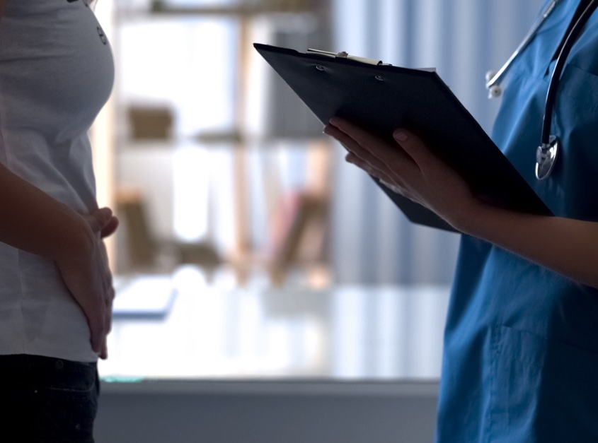 Young lady speaking to doctor while holding lower abdomen in pain