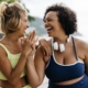 Two happy women in sportswear enjoy their workout routine on the ocean promenade, celebrating with a high-five. Female friends with different body shapes embracing a lifestyle of fitness.