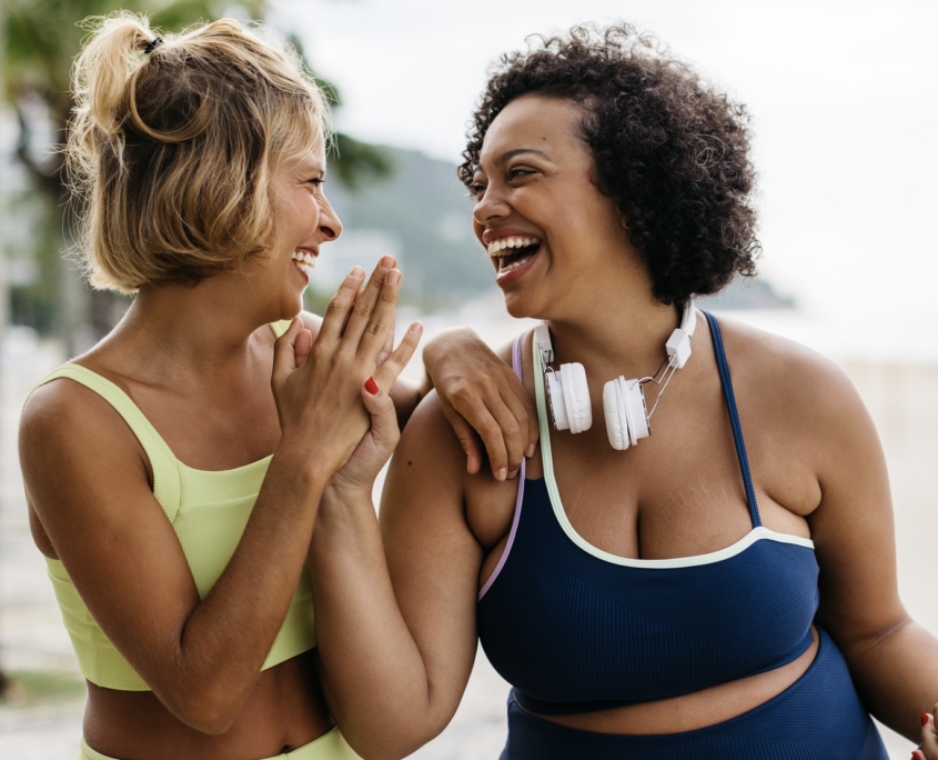 Two happy women in sportswear enjoy their workout routine on the ocean promenade, celebrating with a high-five. Female friends with different body shapes embracing a lifestyle of fitness.
